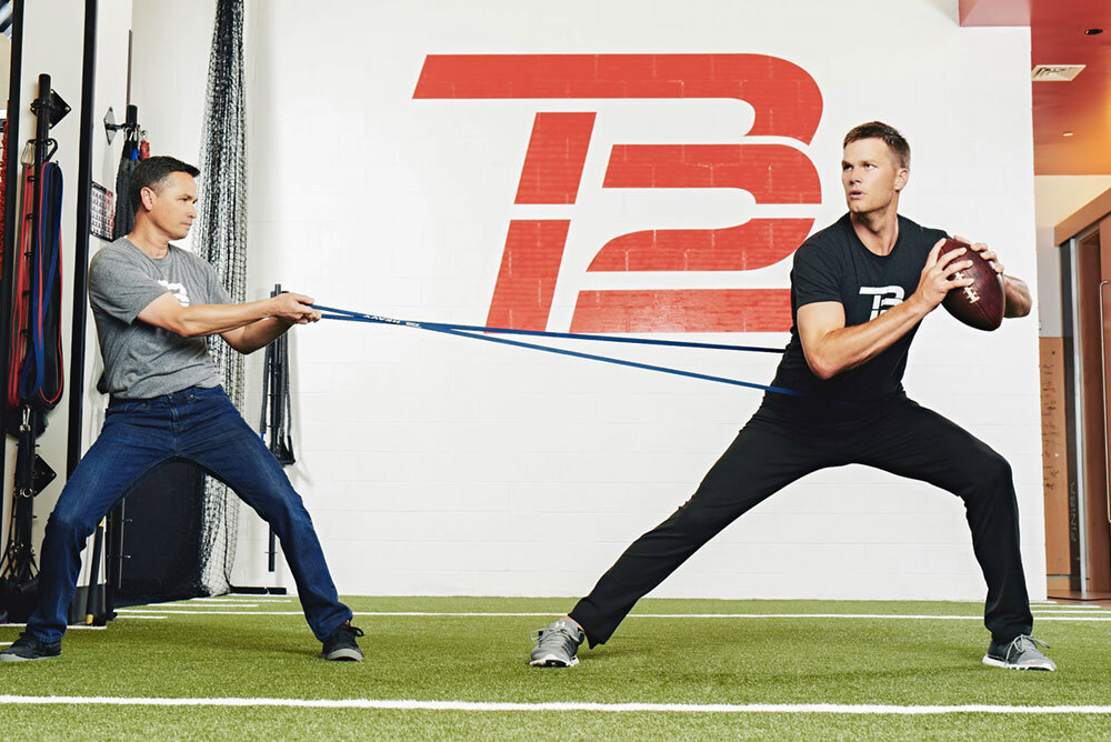 Tom Brady training with resistance bands beneath the TB12 logo